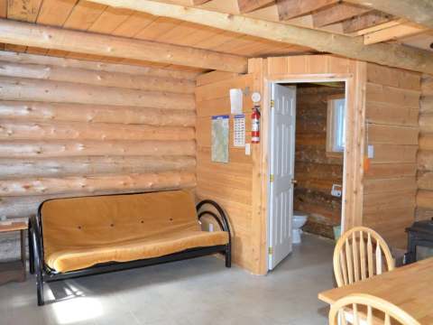 Vue intérieure du camp Refuge avec son coin salon, sa table et l'accès à la salle de bain.