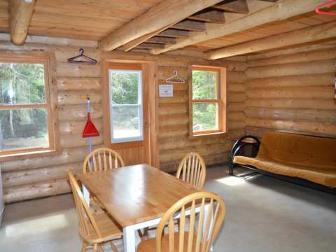 L'espace de vie du camp comprend une table à manger et un canapé-lit en bois rond.