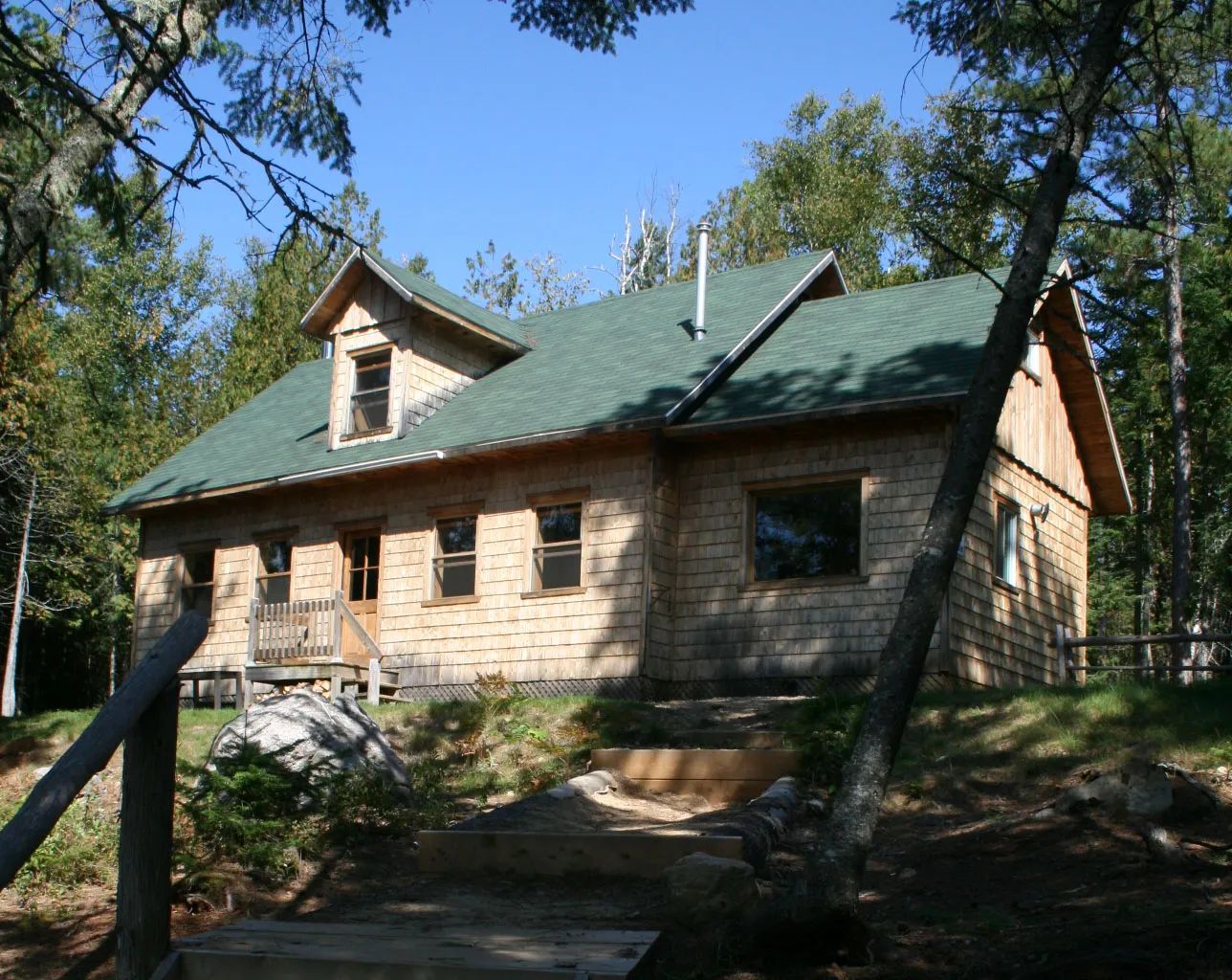 Vue du Chalet Des Pins entouré d'arbres avec un accès par un escalier en bois.