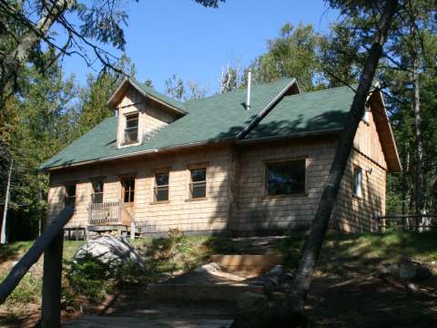 Vue du Chalet Des Pins entouré d'arbres avec un accès par un escalier en bois.