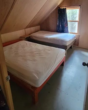 This attic bedroom in the cabin features two single beds with wooden walls.