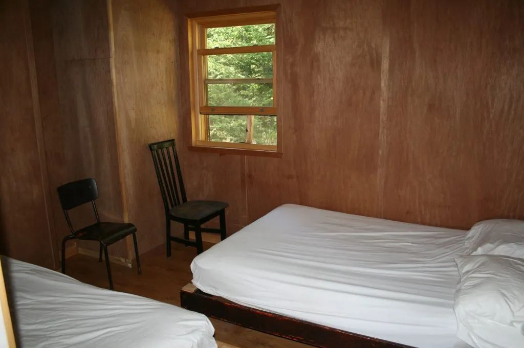Cette chambre rustique du Chalet Des Sables comprend deux lits et une fenêtre donnant sur la forêt.