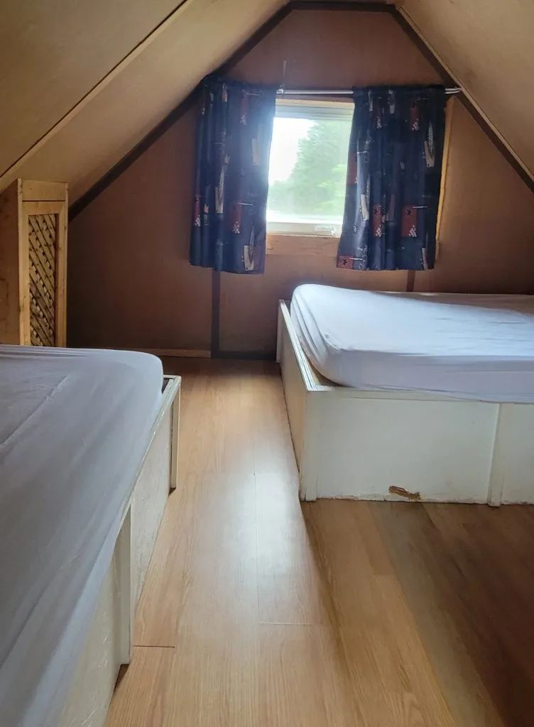 This bedroom under the cabin roof includes two single beds with a view of the forest.