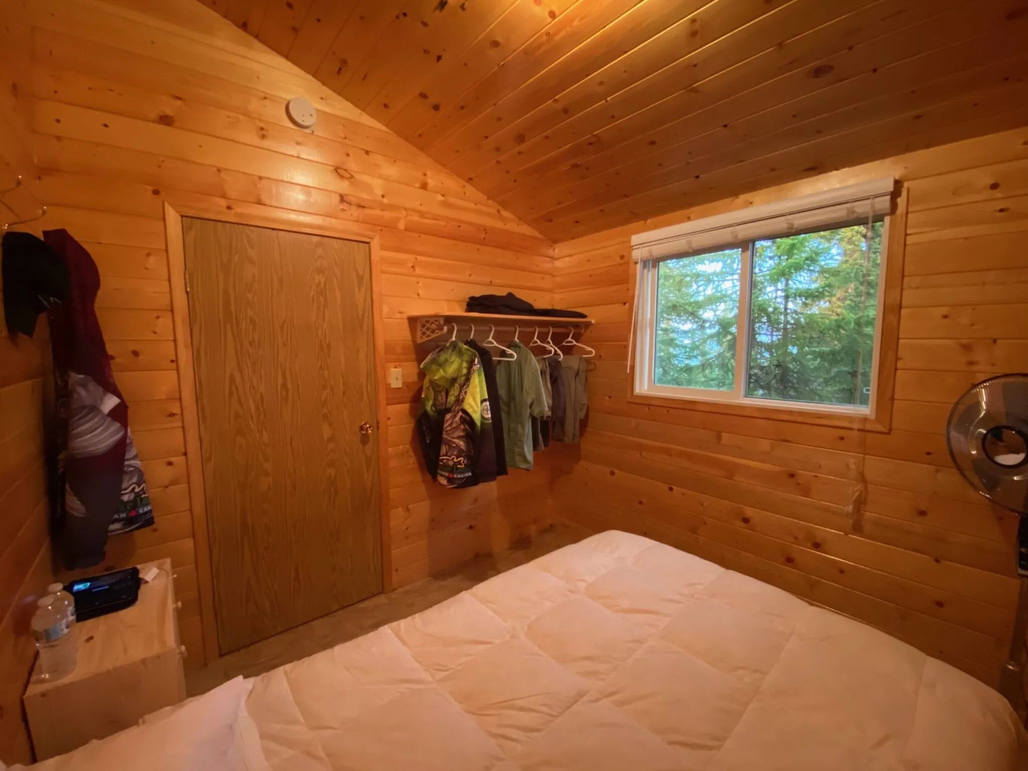 Interior view of a cozy bedroom with wood walls and a window overlooking the forest.